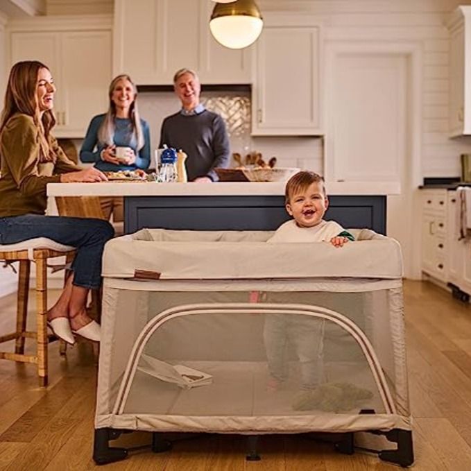 a baby in a crib with two adults and one child sitting at the kitchen table