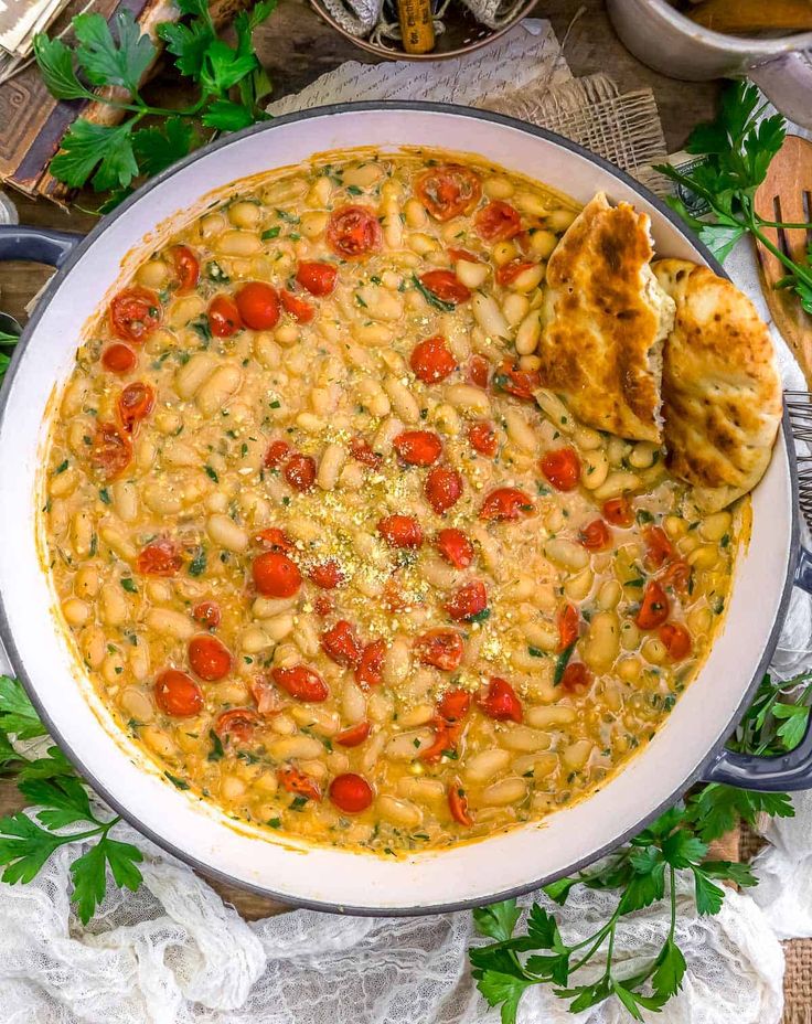 a white bowl filled with pasta and tomatoes on top of a table next to bread