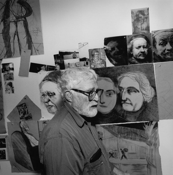 an old man standing in front of a wall covered with pictures and drawings on it