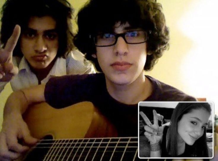 two young men are playing guitar and one is making the peace sign with his fingers