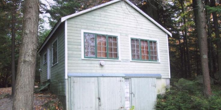 a small white house in the woods with trees around it and leaves on the ground