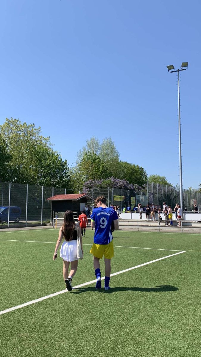 two people walking on a soccer field with one person holding the ball in his hand