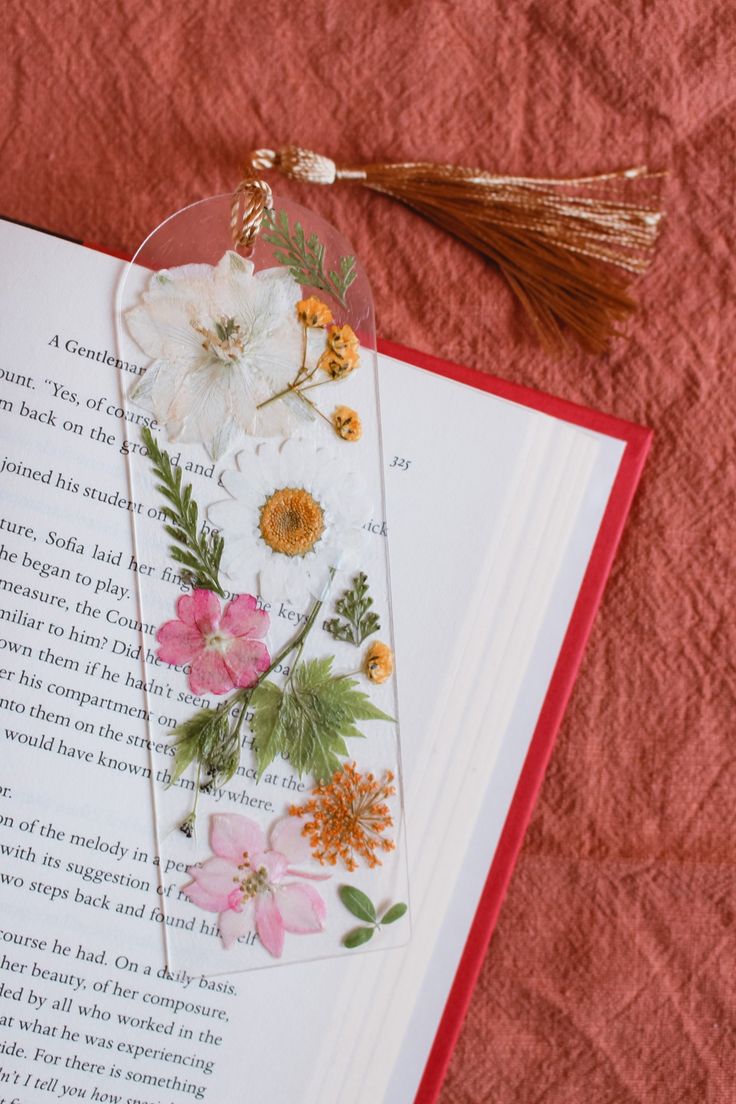 an open book with flowers on it next to a tassel