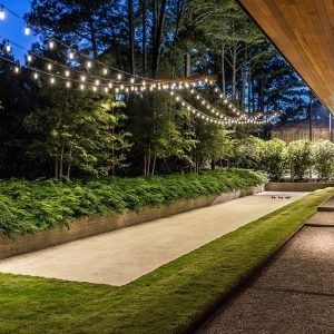 an outdoor patio with string lights strung over the walkway and trees in the back yard