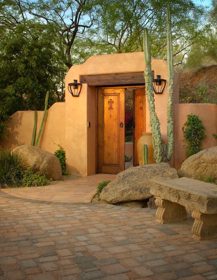 a small adobe style house with a cactus in the front yard and stone benches around it