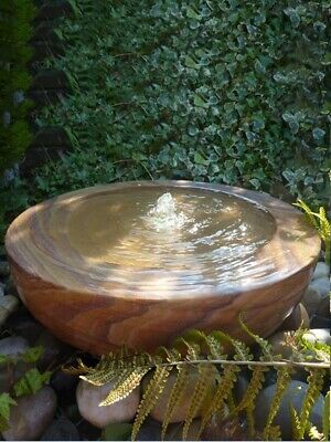 a wooden bowl sitting on top of a pile of rocks next to a green bush