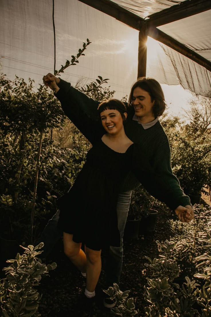 a man and woman are holding hands in the middle of an outdoor area with plants