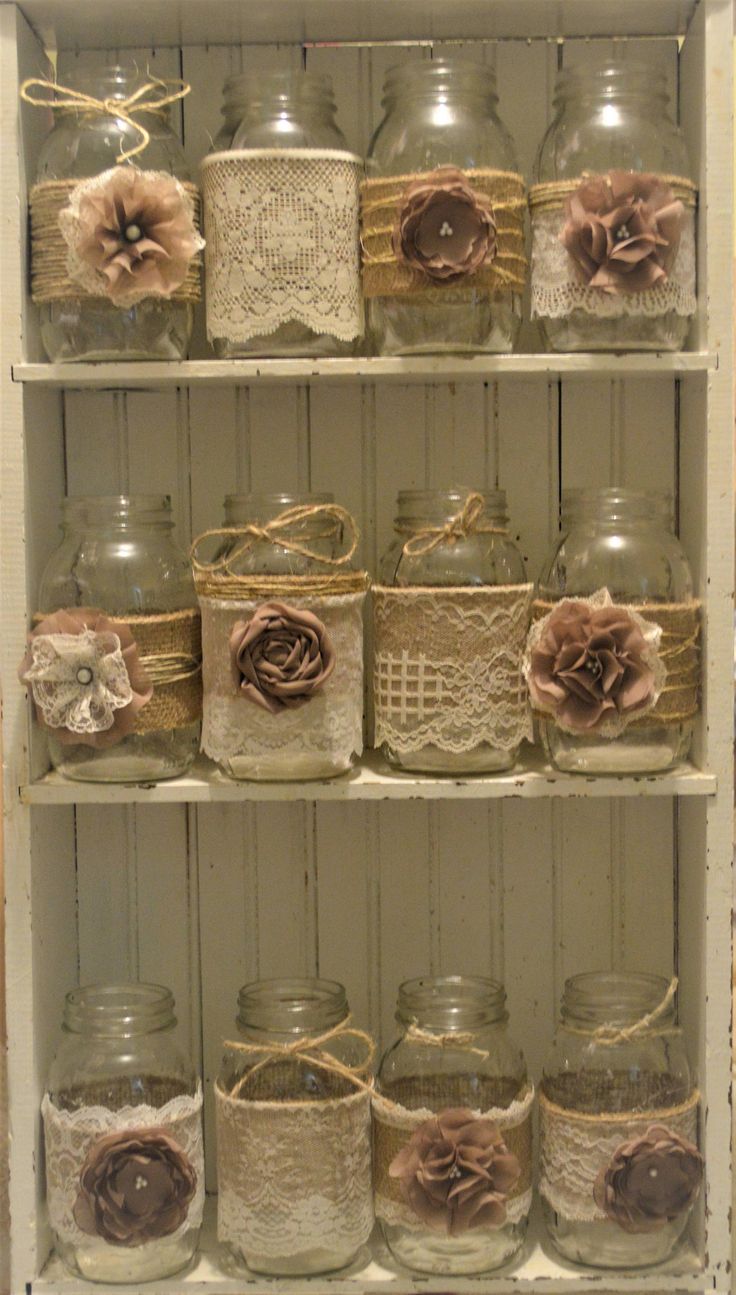 some glass jars with lace and flowers on them are sitting on a shelf in a room