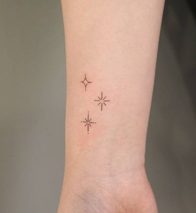 a small wrist tattoo with three stars on the left side of the arm and an arrow in the middle