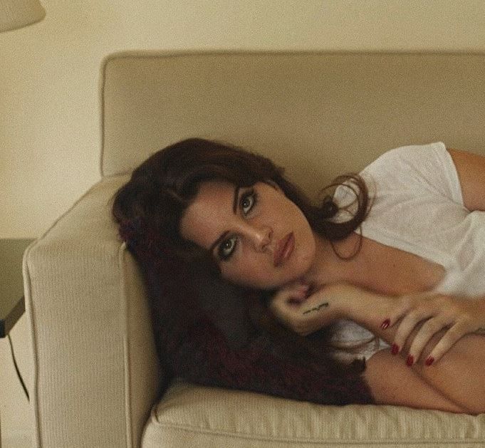 a woman laying on top of a white couch next to a table with a lamp