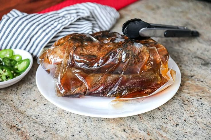 a white plate topped with meat covered in plastic wrap next to a bowl of salad