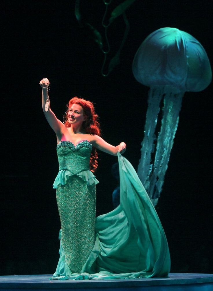 a woman in a green dress is dancing with jellyfishs on the water behind her