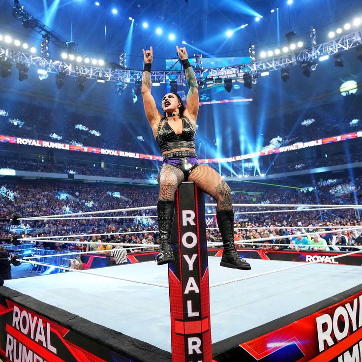 a woman sitting on top of a wrestling ring holding her arms up in the air