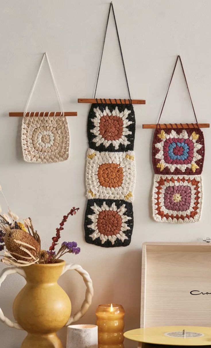 three crocheted wall hangings on a white wall next to a yellow vase