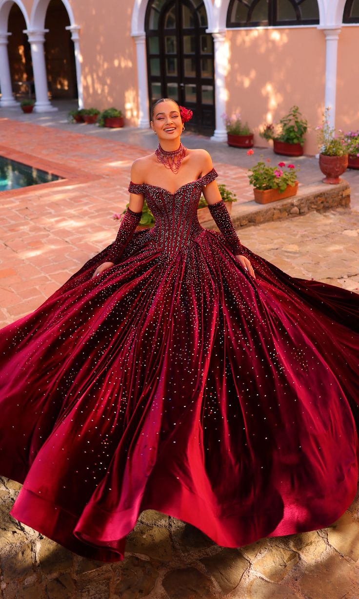 In this off-the-shoulder velvet quinceañera dress, prepare for a glamorous night of celebration. Soft and sumptuous, the lavish velvet fabric on this quince ball gown is the perfect backdrop for sparkling bead and stone accents. The corset bodice features supportive boning and an adjustable lace-up back. Along with a matching necklace, this beaded quince dress has elbow sleeves you can slip on to level up the classy elegance even further. Mesmerize the masses when you step out wearing this off-t Red Corset Ball Gown, Maroon Quinceanera Dresses, Fantasy Ball Gowns, Quince Outfit, Dragon Bedroom, Velvet Wedding Dress, Fantasy Ball, Red Ball Gowns, Quince Themes