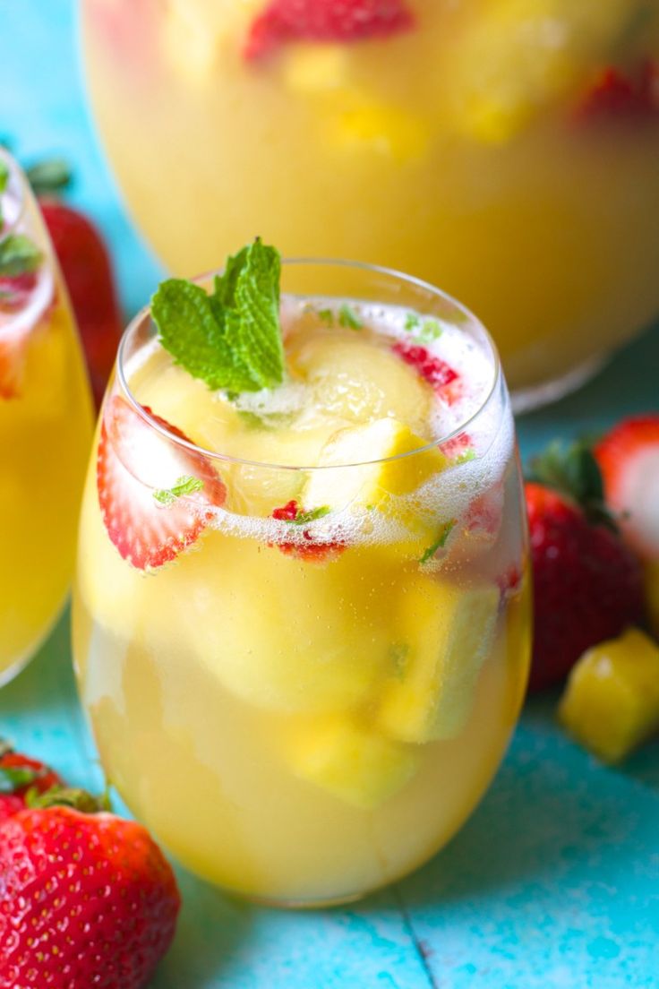 two glasses filled with lemonade and strawberries on top of a blue tablecloth