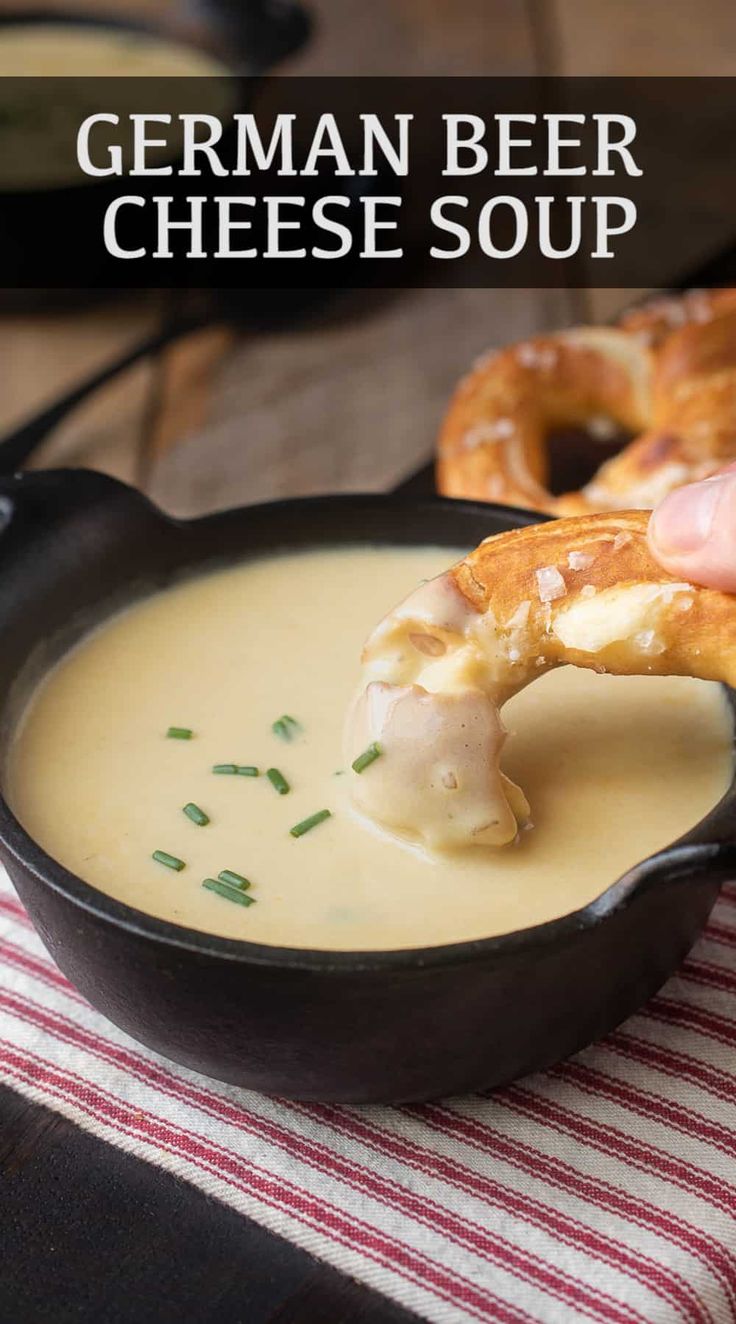 a person dipping cheese into a bowl of soup with pretzels in the background