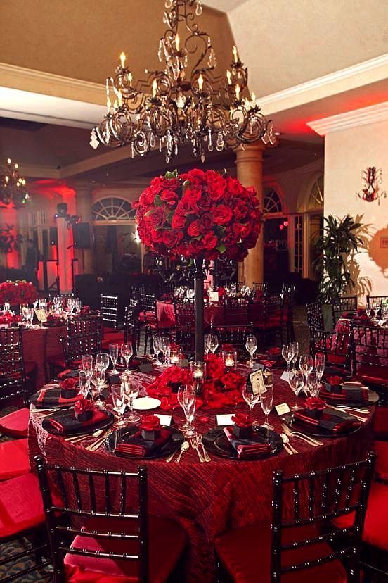 a dining room set up for a formal function with red flowers on the table and centerpieces