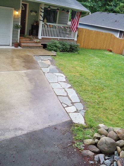 a driveway with rocks and grass in front of a house that has a flag on it