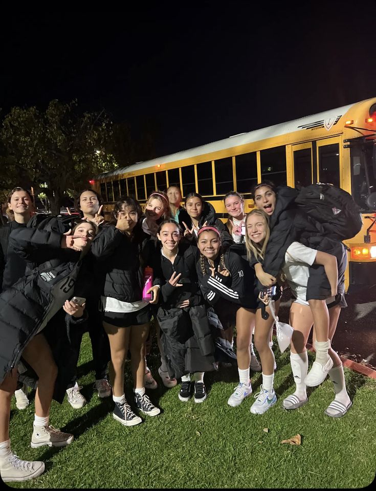 a group of girls standing in front of a school bus at night with their arms around each other