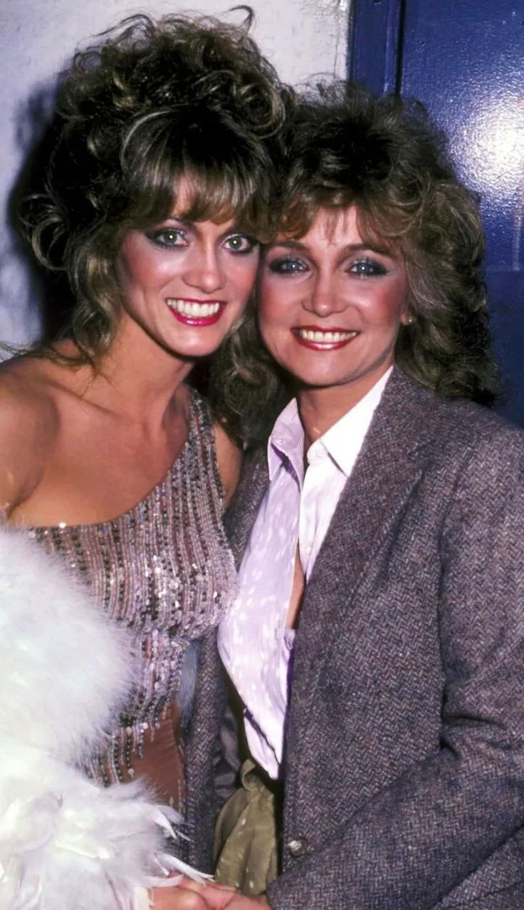 two women are posing for the camera together in front of a blue door and white feathers