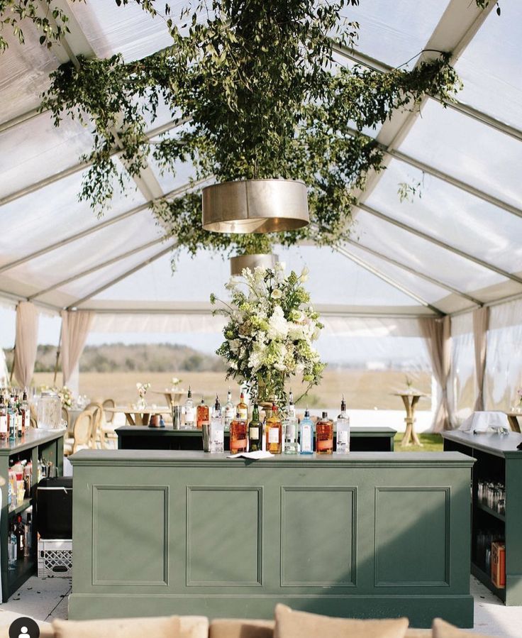 an outdoor bar with lots of bottles and flowers on the top shelf in front of it