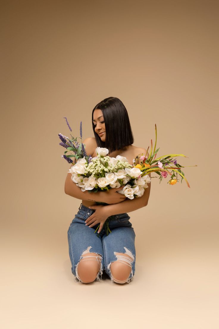 a woman sitting on the ground with flowers in her lap and ripped jeans around her ankles