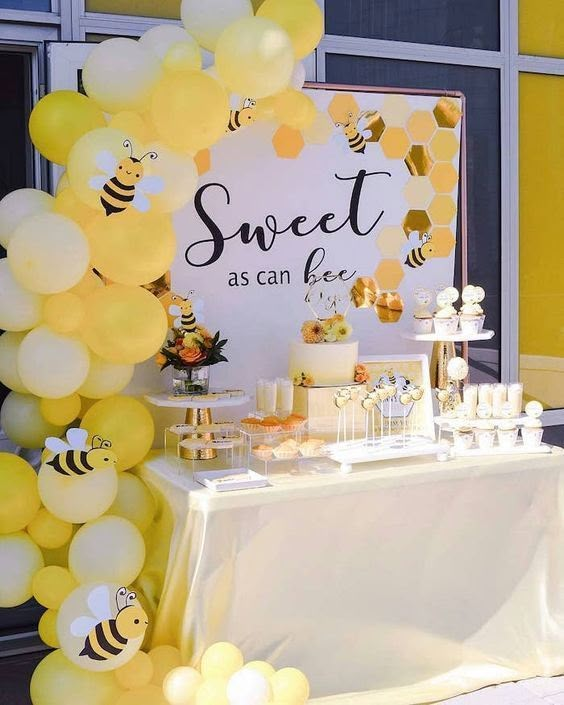 a table topped with lots of yellow balloons and honeycombs next to a sign that says sweet as can bee