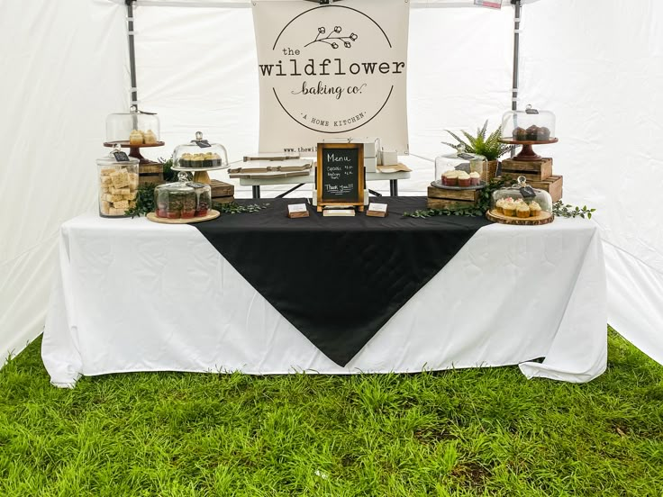 a table topped with cakes and desserts under a white tent covered in black cloth