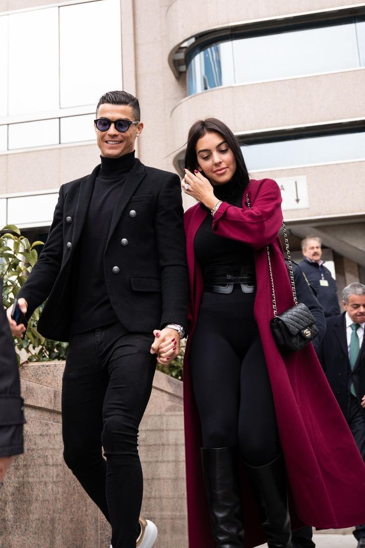 a man and woman holding hands walking down the street with other people in the background