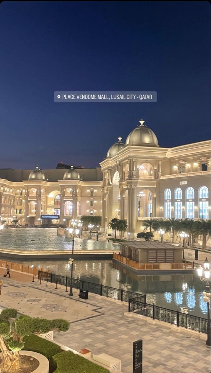 the building is lit up at night with lights on it's roof and water fountain in front