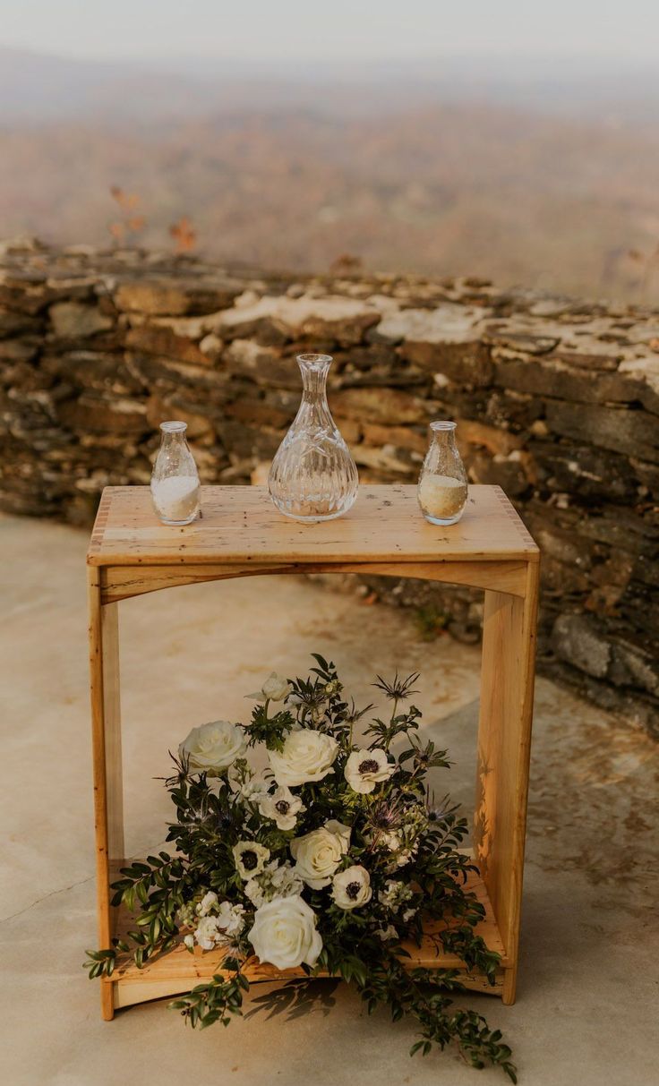 a table with flowers and vases on top of it next to a stone wall