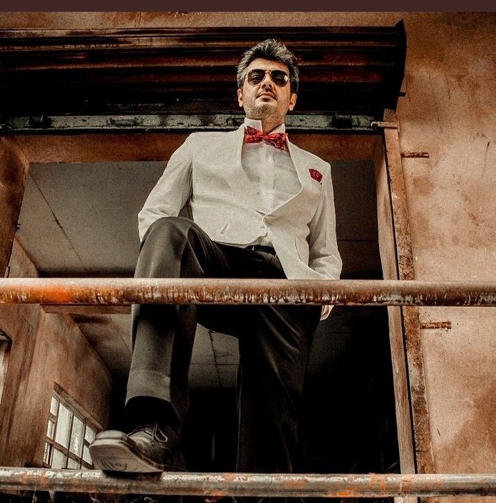 a man in a suit and bow tie is sitting on a balcony railing looking off into the distance