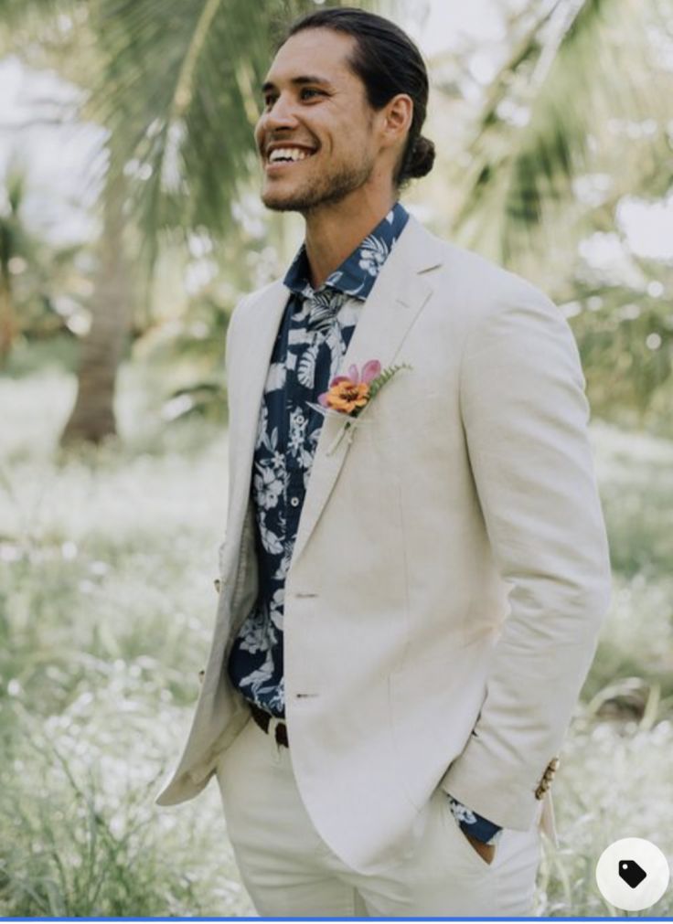 a man in a white suit and flowered shirt smiles while standing in the grass