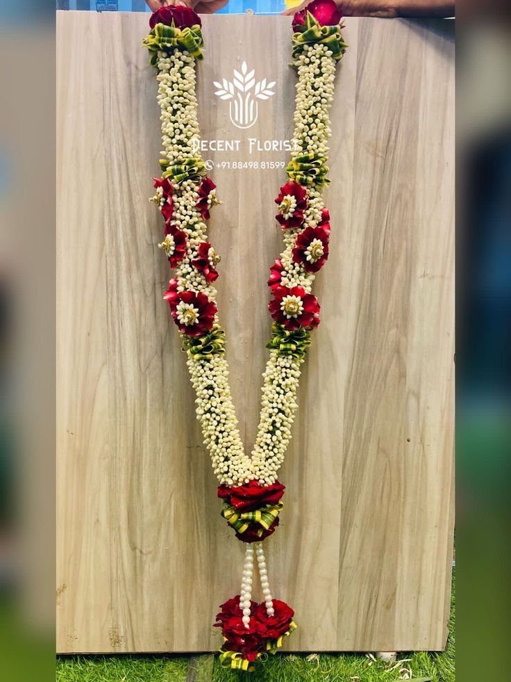 a long flower garland with red and white flowers hanging from it's sides on a wooden wall