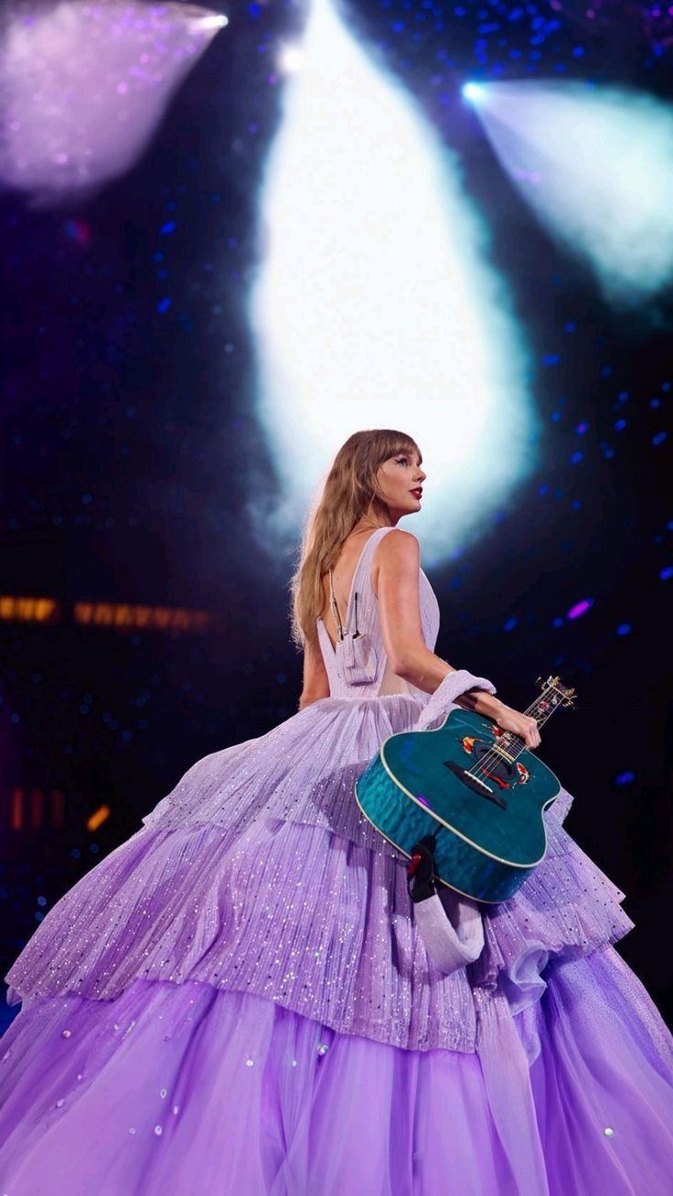 a woman in a purple dress is holding a green guitar case and looking off into the distance