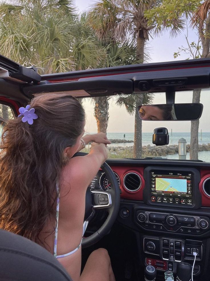 a woman sitting in the driver's seat of a car with palm trees behind her