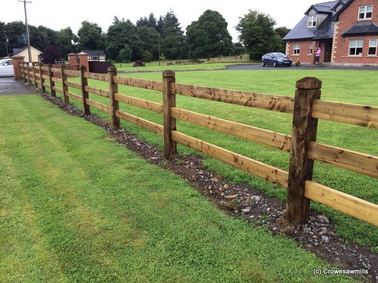 a wooden fence in the middle of a grassy field next to a red brick house