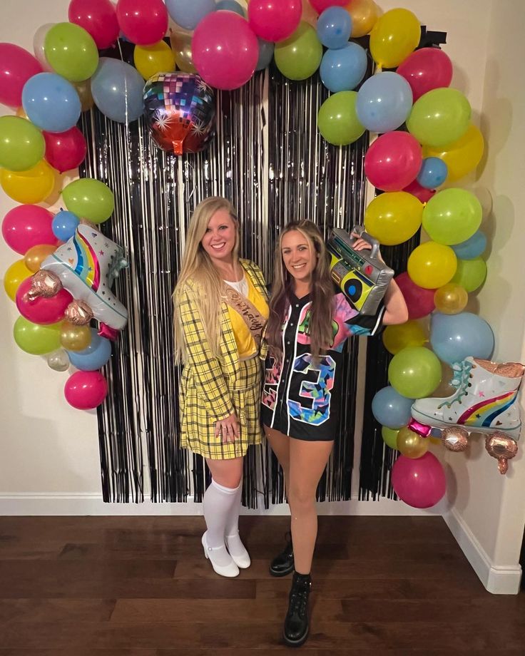 two women standing next to each other in front of a balloon arch with roller skates on it