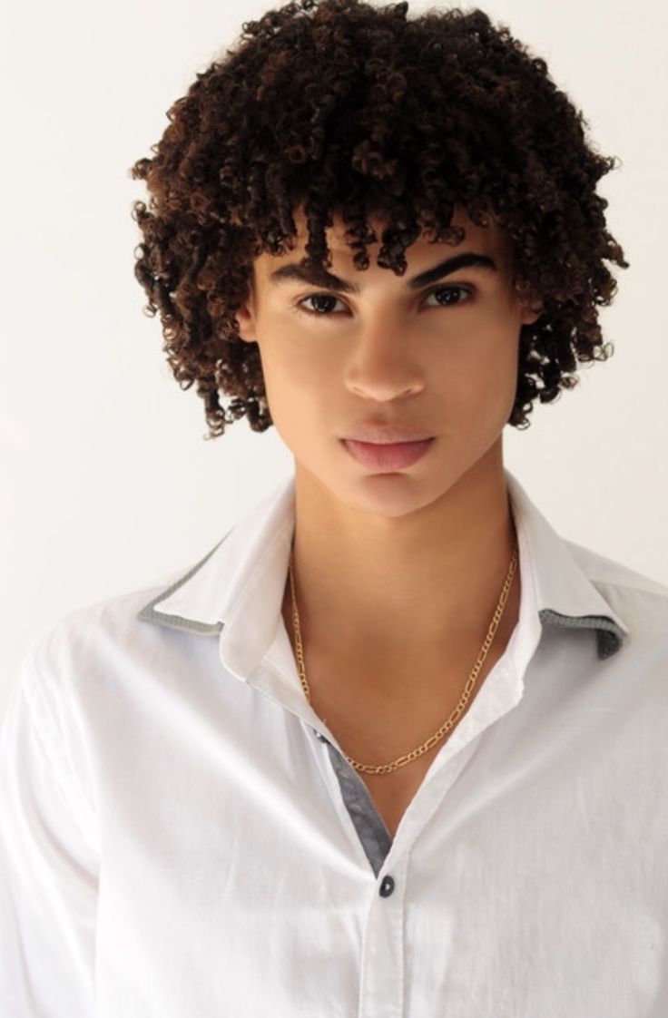 a close up of a person wearing a white shirt and gold necklace with curly hair