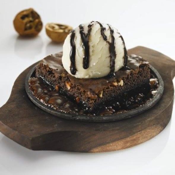 a piece of cake with ice cream and chocolate on top is sitting on a wooden platter