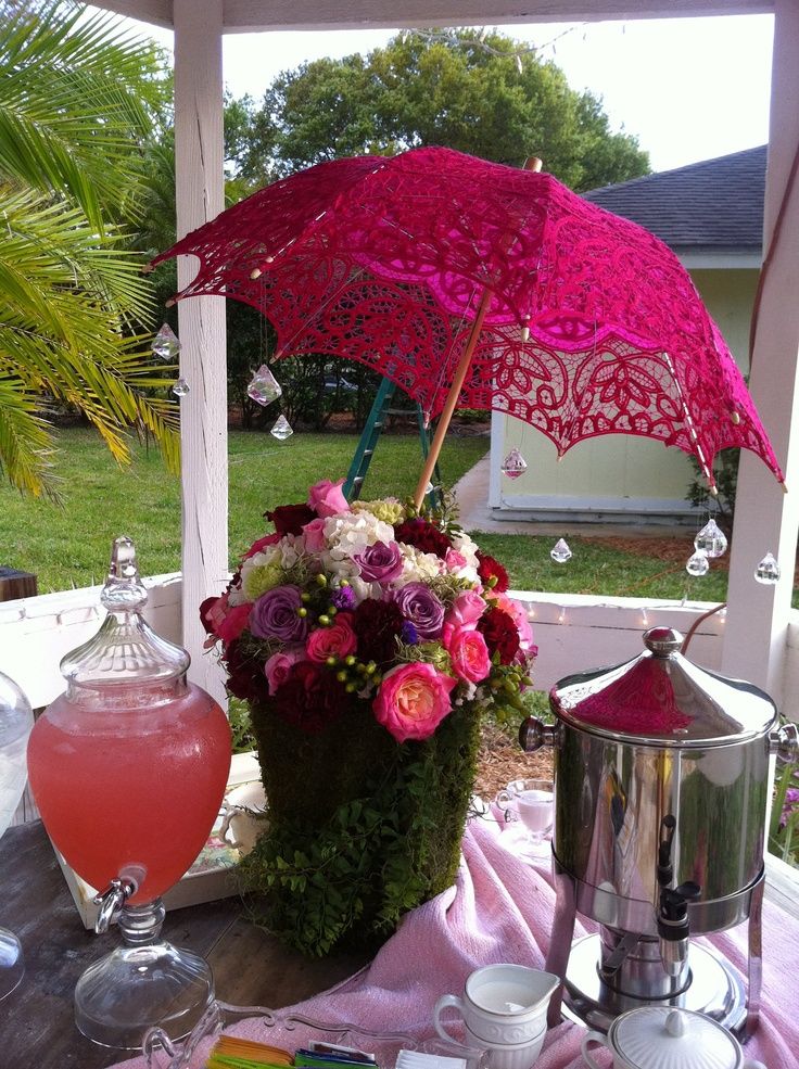 a table topped with a pink umbrella next to a metal pot filled with flowers and drinks