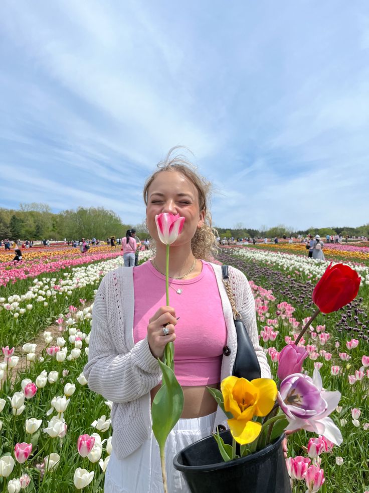 a woman standing in a field with tulips and holding a large plastic lollipop