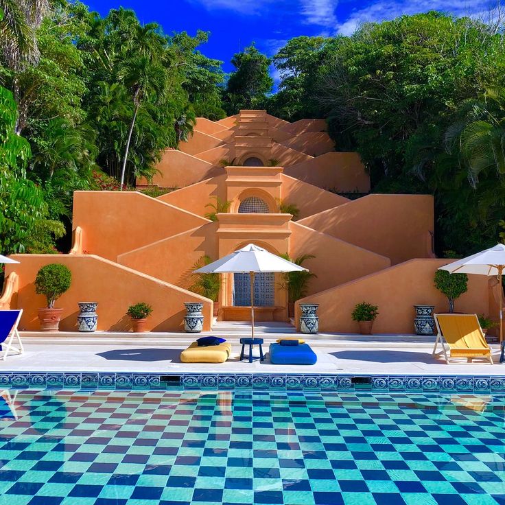 an outdoor swimming pool with lounge chairs and umbrellas in front of a building that looks like a desert