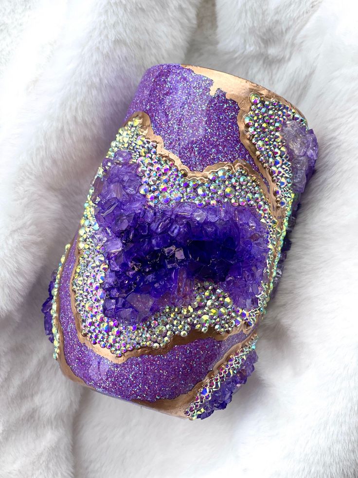 a purple and gold cuff with lots of crystals on it's side, sitting on a white fur covered surface