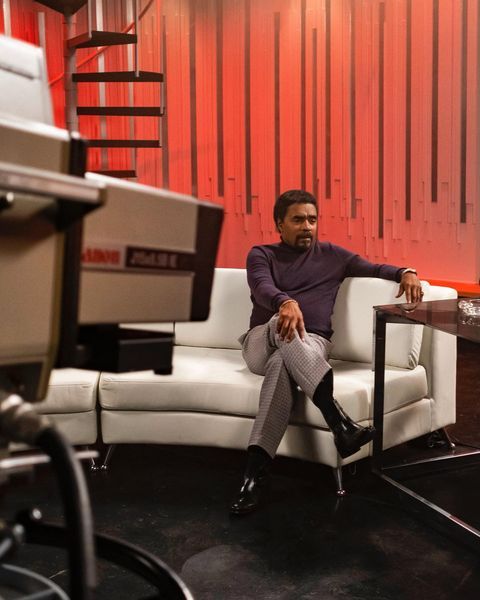 a man sitting on top of a white couch in front of a red wall next to a table