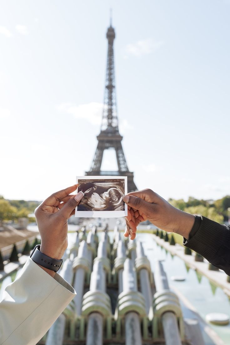 two hands holding up an old photo in front of the eiffel tower