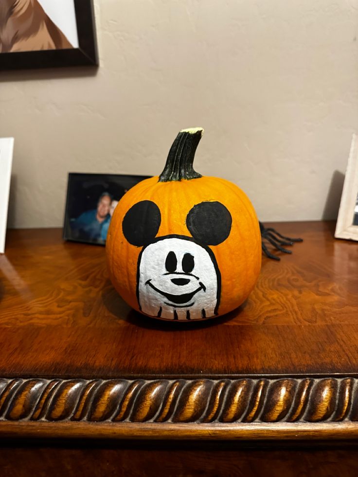 a pumpkin with a face painted on it is sitting on a table next to pictures