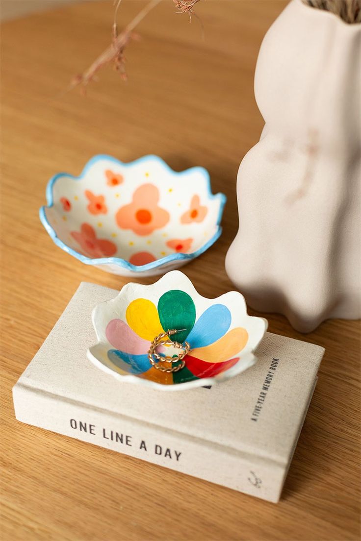 a ceramic flower sitting on top of a book next to a vase