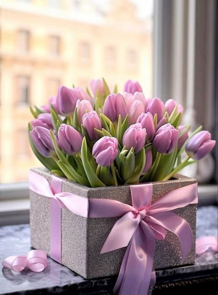 pink tulips are in a gray box on a window sill with ribbon